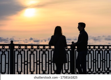 Two young people are talking while standing at sunset against the backdrop of the sea landscape