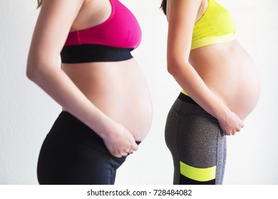Two young pregnant women doing yoga exercises at studio