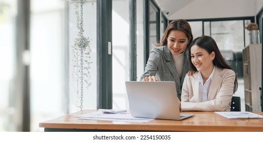 Two young pretty asia business woman in suit talking together in modern office workplace, Thai woman, southeast asian, looking on laptop together - Powered by Shutterstock