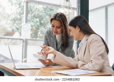 Two young pretty asia business woman in suit talking together in modern office workplace, Thai woman, southeast asian, looking on laptop together - Shutterstock ID 2254881083