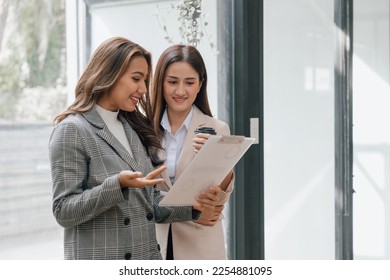 Two young pretty asia business woman in suit talking together in modern office workplace, Thai woman, southeast asian, Standing - Shutterstock ID 2254881095
