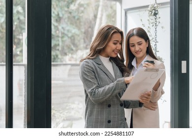 Two young pretty asia business woman in suit talking together in modern office workplace, Thai woman, southeast asian, Standing - Shutterstock ID 2254881107