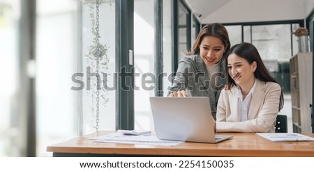 Two young pretty asia business woman in suit talking together in modern office workplace, Thai woman, southeast asian, looking on laptop together