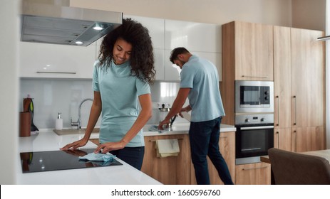 Two young professional cleaners in uniform working together in the kitchen. Happy afro american woman cleaning electric stove, young caucasian man wiping kitchen table. Cleaning services concept - Powered by Shutterstock