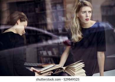 Two Young Professional Women In A Library Reading Books. Look Outside The Window. Education Concept