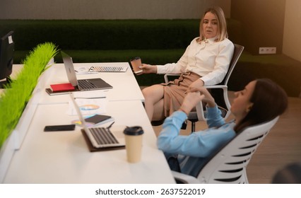 Two young professional women relax at a modern open-plan office. One sips coffee while reclining in her chair; the other works on a laptop amid plants and color swatches.
 - Powered by Shutterstock - Get 15% off with code: PIKWIZARD15