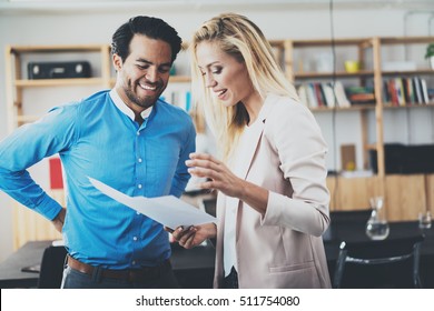 Two Young Professionals Making A Great Business Discussion In Modern Office.Successful Confident Hispanic Businessman Talking With Woman Partner. Horizontal, Blurred Background