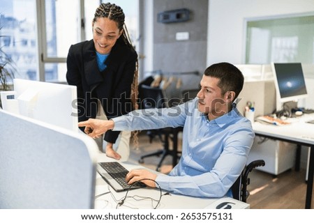 Two young professionals, one using a wheelchair, are working together on a computer project in a modern coworking office