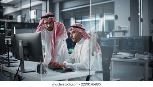 Two Young Saudi Software Engineers Use Desktop Computer to Discuss a Technological Project in a Modern Industrial Office. Arab Scientists Work in Research and Development Center