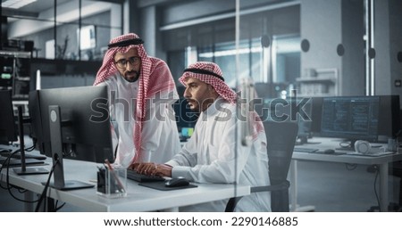 Two Young Saudi Software Engineers Use Desktop Computer to Discuss a Technological Project in a Modern Industrial Office. Arab Scientists Work in Research and Development Center