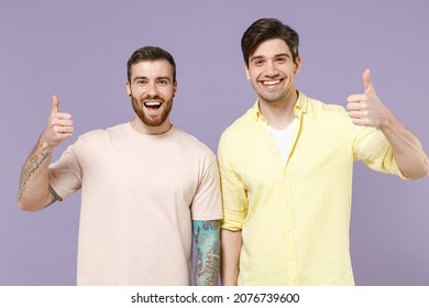Two young smiling cheerful happy cool men friends together in casual t-shirt tattoo translate fun show thumb up gesture isolated on purple color background studio portrait People lifestyle concept. - Shutterstock ID 2076739600