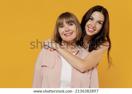 Two young smiling satisfied daughter mother together couple women wearing casual beige clothes looking camera hug isolated on plain yellow color background studio portrait. Family lifestyle concept