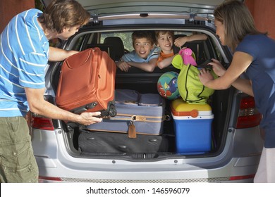 Two Young Sons Watching Parents Load Luggage In Car Trunk