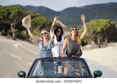 Two Young Spanish Girls Having Fun While Standing In A Cabriolet Car On A Sandy Beach