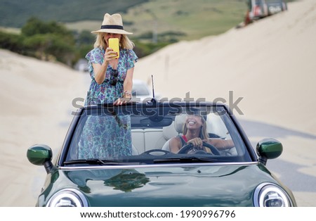Two young Spanish girls having fun in a cabriolet car on a sandy beach
