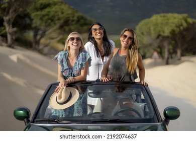 Two Young Spanish Girls Standing In A Cabriolet Car And Smiling Happily On A Sandy Beach