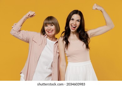 Two young strong sporty fitness daughter mother together couple women in casual beige clothes show biceps muscles on hand demonstrating strength power isolated on plain yellow color background studio