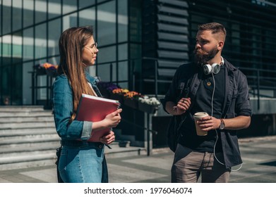 Two Young Students Meeting In Front Of The Faculty While Holding Books And Coffee Takeaway And Going To The Lecture