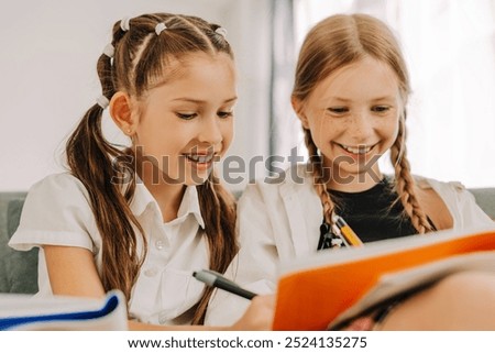 Two young students are sitting side by side, collaborating on their homework and sharing ideas with smiles on their faces