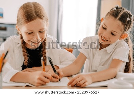 Two young students are smiling while working together on a school project at home, writing in their notebooks