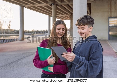 Two young students using a digital tablet for learning or social media outdoors