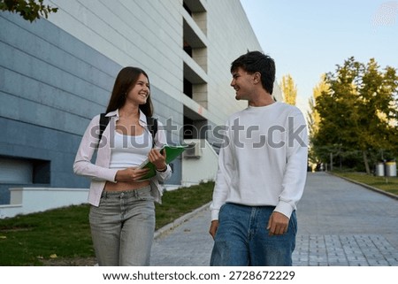 Two young students walking and talking on a modern university campus, sharing a laugh and enjoying student life