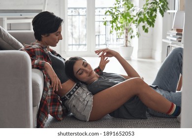 Two Young Stylish Cool Diverse Women Lesbian Lgbtq Couple Dating In Love Relaxing At Home Together Sitting On Floor Enjoying Intimate Tender Sensual Moment Touching Hands Chilling In Apartment.