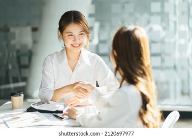 Two Young Successful Colleagues In Formal Wear Having Tea And Discussing Organizational Moments By Table In Cafe, Asian Business Woman Meeting And Brainstorm Concept.