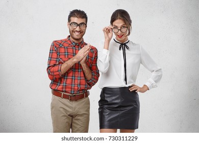 Two young teachers in spectacles have intriguing look, going to teach you, or give lesson. Happy male and female colleagues wear formal clothes, come to conference, smile happily into camera