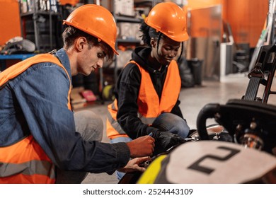 Two young technicians in hard hats and vests working on go-kart maintenance inside a workshop. - Powered by Shutterstock