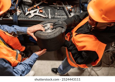 Two young technicians in safety gear closely examining a go-kart tire in a workshop setting. - Powered by Shutterstock