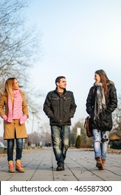 Two young teenage girls and one guy walking down the street and talk