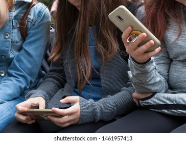 Two young teenage girls sitting holding smartphones in their hands. Teens, kids playing around, checking their phones Phone addiction or young preteens using modern technology in everyday life concept