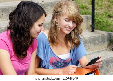 Two Young Teenager Students Using Their Cell Phone And Laughing, Perfect For Networking, Social Media And The Likes.