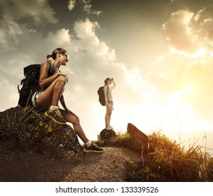 Two young tourists with backpacks relaxing on rocks and enjoying sunset - Powered by Shutterstock