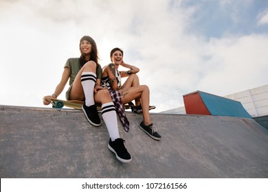 Two young urban girls in skate park laughing and having fun. Two female friends sitting on a long board. - Powered by Shutterstock