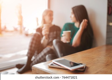 two young woman chatting in a coffee shop. Two friends enjoying coffee together. Their smartphones lying in pile on table on foreground - Shutterstock ID 764471821