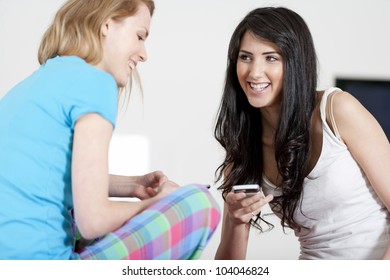Two young woman chatting and using their mobile phones at home
