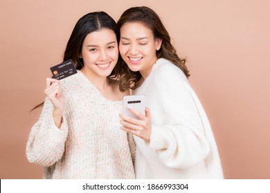 Two Young Woman With Mobile Phone And Credit Card Having Fun Together Portrait Isolated On Brown Color Background