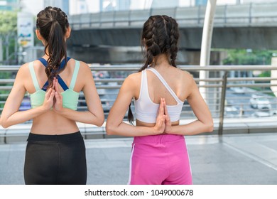 Two young woman posing basic yoga pose in public exercise area of big city.