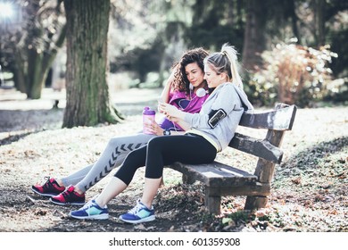 Two young woman sitting on bench at the park and relaxing after jogging,early in the morning.Sharing the earphones and listening to music. - Powered by Shutterstock