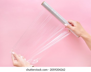 Two Young Woman's Hands Holding Plastic Wrap On Pink Background Horizontal Copy Space