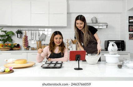 Two young women in an apron make dessert in the kitchen while looking at online recipe guide book on tablet computer. - Powered by Shutterstock