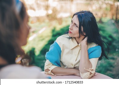 Two young women argue in cafe. Emotional speech. Woman with an indignant look looks at her friend sitting at a round table in a cafe, an angry beautiful girl in a cafe with her friend. Emotion. 
