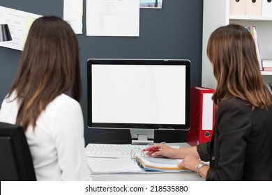 Two Young Women In A Business Team Working Together On A Desktop Computer In The Office, Over The Shoulder View Of The Blank Screen