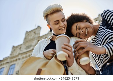 Two young women in casual attire holding coffee cups, engaged in conversation and sharing a moment of connection. - Powered by Shutterstock