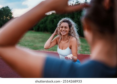 Two young women chatting and laughing on a running track, they are preparing for their training, one girl tying her hair back. They are dressed in athletic wear. - Powered by Shutterstock