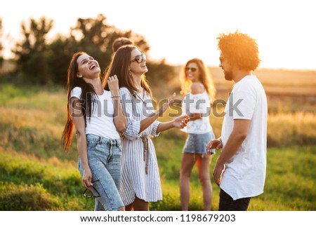 Two young women chatting and laughing with young curly man outdoor.