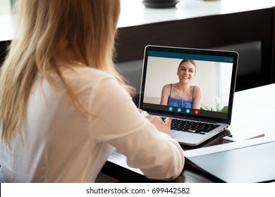 Two young women chatting online by making video call on laptop, using videoconferencing app for communication with distance friend, studying online course, virtual learning, close up rear view