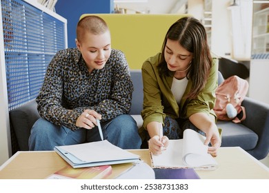 Two young women collaborating at work reviewing documents in modern office. One woman with short hair in leopard print blouse and other with long hair in green jacket - Powered by Shutterstock